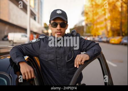 Polizeibeamter in Uniform posiert auf dem Streifenwagen. Polizist beschützen das Gesetz. COP arbeitet an der städtischen Straßen-, Ordnungsungs- und Justizkontrolle Stockfoto