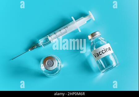 Glasfläschchen mit Label-Impfstoff und hypodermischer Spritzennadel in der Nähe, Ansicht von oben auf cyanfarbenem Hintergrund. Stockfoto