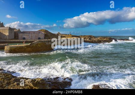 PORTSOY ABERDEENSHIRE SCOTLAND 17C BIETET EINEN WINDIGEN TAG MIT WELLEN AUF FELSEN UND EINER HAFENMAUER Stockfoto