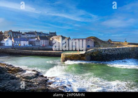 PORTSOY ABERDEENSHIRE SCOTLAND 17C BIETET EINEN WINDIGEN TAG MIT WELLEN AUF DEN FELSEN UND EINER HAFENMAUER Stockfoto