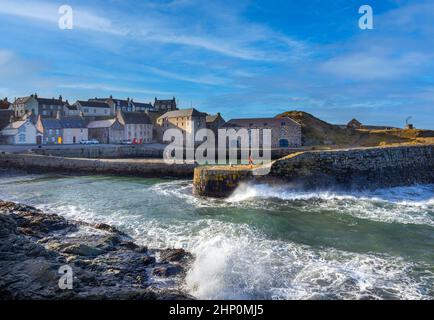 PORTSOY ABERDEENSHIRE SCHOTTLAND DER HAFEN VON 17C AN EINEM WINDIGEN TAG MIT WELLEN AUF DEN FELSEN UND EINER HAFENMAUER Stockfoto