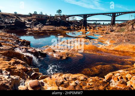 Felsen, die durch das Wasser des Rio Tinto, einem berühmten Bergbaufluss, der durch die Provinz Huelva in der autonomen Gemeinde Andal fließt, orange gefärbt sind Stockfoto