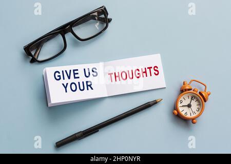 Text auf Notizblock mit Lesebrille, Stift und Wecker auf blauem Hintergrund - geben Sie uns Ihre Gedanken. Stockfoto