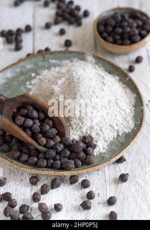 Teller und Holzlöffel aus schwarzem Kichererbsenmehl und Bohnen lassen sich auf dem weißen Holztisch verstauen. Traditionelle Bohnen aus Apulien und Basilikata in Italien Stockfoto