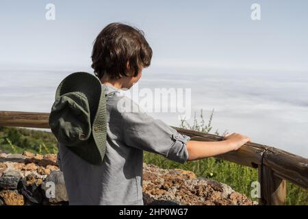 Der Junge steht auf einer Aussichtsplattform über den Wolken und blickt in die Ferne. Stockfoto