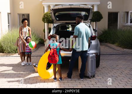 Glückliche afroamerikanische Familie, die Gepäck in den Kofferraum lädt, während sie zum Picknick geht Stockfoto