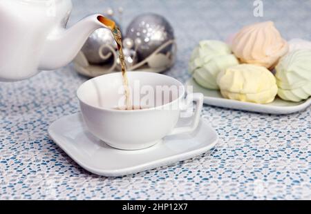 Tea Party Zeit. Die Gastgeberin gießt Tee in Tassen aus dem Wasserkocher, in einem Stück mit köstlichen frischen Marschmalchen, auf einem festlichen Tisch Stockfoto