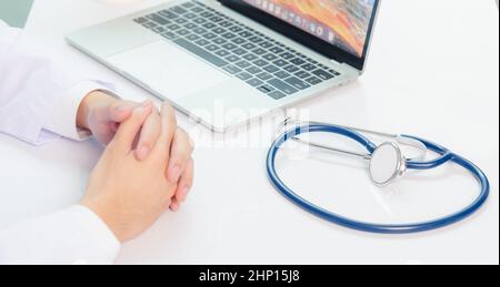 Mediziner arbeitet am Schreibtisch. Nahaufnahme des Stethoskops. Arzt Mann Videoanruf sitzen Hand in Hand und hören Patienten erklären auf der Vorderseite Laptop Comput Stockfoto