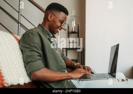 Afroamerikanischer Student, der auf dem Sofa sitzt und auf dem Laptop tippt, um für Online-Prüfungen zu lernen Stockfoto