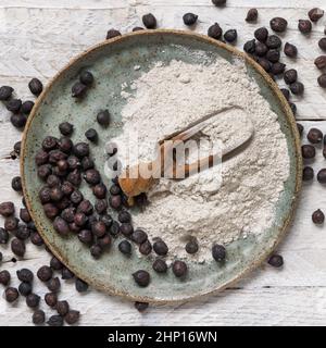 Teller und Holzlöffel aus schwarzem Kichererbsenmehl und Bohnen von oben auf weißem Holztisch. Traditionelle Bohnen aus Apulien und Basilikata in Italien Stockfoto