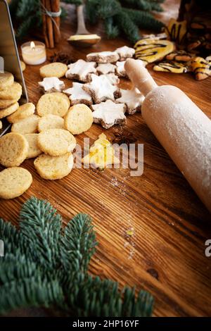 Verschiedene hausgemachte weihnachtskekse und eine Teigwalze auf einem Holztisch. Vertikaler Hintergrund mit kurzer Schärfentiefe für das süße weihnachtsbacken. Stockfoto