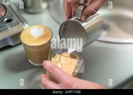 Der Barista bereitet Cappuccino zu, gießt geschlagene Milch in ein Glas Espresso. Stockfoto