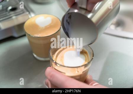 Ein Mann kocht zu Hause Cappuccino, gießt Milch aus dem Krug in ein Glas. Stockfoto