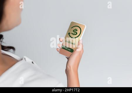 Beschnittene Ansicht einer verschwommenen Frau mit Mobiltelefon und Cashback auf dem Bildschirm, isoliert auf Grau Stockfoto