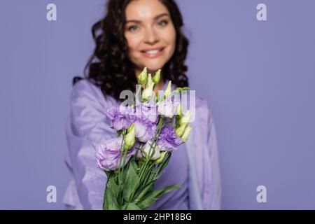 Glückliche verschwommene Frau hält Blumenstrauß isoliert auf lila Stockfoto