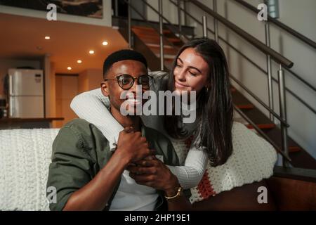 Afroamerikanische männliche und kaukasische Freundin zeigt Zuneigung auf der Couch, während sie sich umarmt Stockfoto