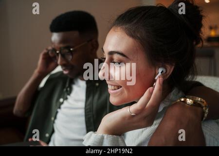 Biracial Paar sitzt auf dem Sofa und hört Musik mit Ohrhörern Stockfoto