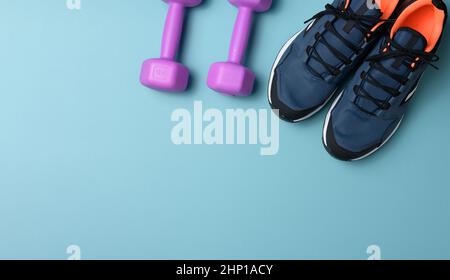 Paar blaue Sneaker und lila Kurzhanteln auf blauem Hintergrund, Sport. Speicherplatz kopieren Stockfoto