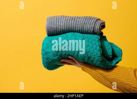 Frau mit einem Stapel gestrickter, gefaltetem Pullover auf gelbem Hintergrund. Wäsche waschen Stockfoto