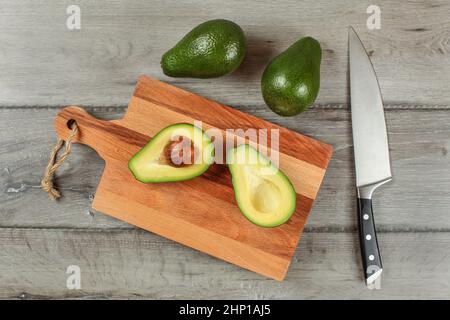 Table Top - avocado Halbieren auf Holz Schneidebrett, Kochmesser, ganze zwei grüne Birnen oben. Stockfoto