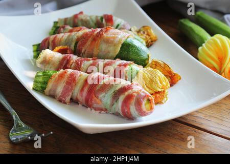 Gegrillte Zucchini-Pommes frites in einem Speck auf weißem Teller gewickelt. Stockfoto