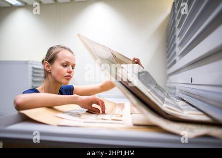 Hübsche, junge Frau, die alte Karten in Archiven studiert Stockfoto