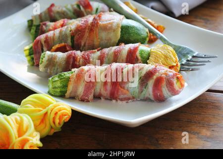 Gegrillte Zucchini-Pommes frites in einem Speck auf weißem Teller gewickelt. Stockfoto