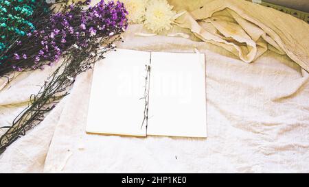 Leeres weißes Papier Notizbuch und Blumendekoration. Grußkarte auf weißem, natürlichem Leinenhintergrund. Draufsicht. Speicherplatz kopieren. Stockfoto