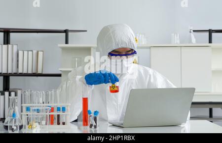 Epidemiologische Forscher in Virusschutzkleidung, die Chemikalien nach Formeln aus Computern mischt. Arbeitsatmosphäre in der Chemica Stockfoto