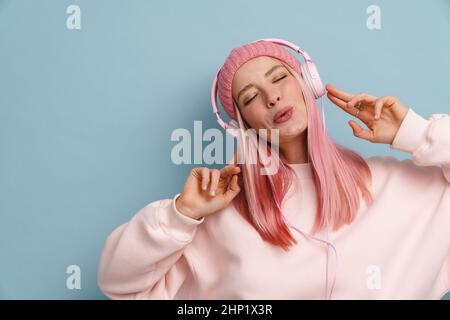 Junge Frau singt beim Musikhören mit Kopfhörern, die über der blauen Wand isoliert sind Stockfoto