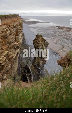 Eine riesige kaputte Felssäule, die auf der Klippe gestrandet war, wartete nur darauf, am Strand zu bröckeln. Stockfoto