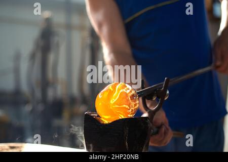 Nahaufnahme der Hände eines Glasbläsers, der mit geschmolzenem Glas arbeitet, traditioneller Handarbeit. Stockfoto