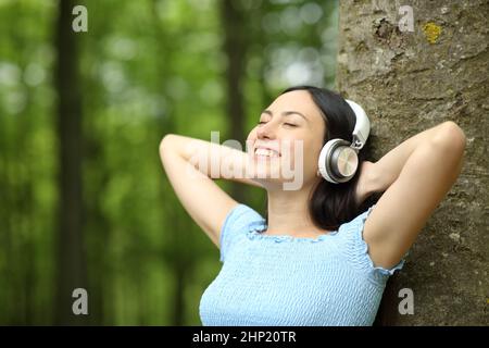 Glückliche asiatische Frau, die in einem Park Kopfhörer trägt und Musik hört Stockfoto