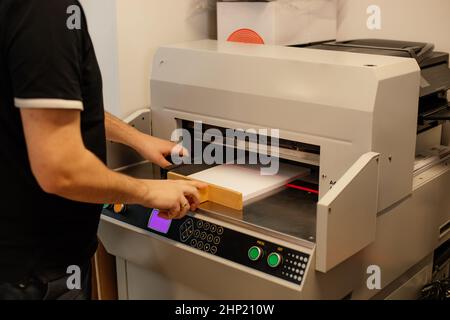 Beschnittenes Bild Mann Arbeiter Hände Papierschneider Maschine, Guillotine Offset. Herstellung. Stopfer des Papierstapels. Stockfoto