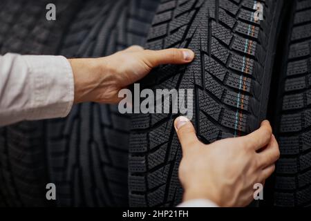 Nahaufnahme der Hand eines Mannes mit Autoreifen im Autogeschäft. Mann, der neue Winterreifen wählt Stockfoto