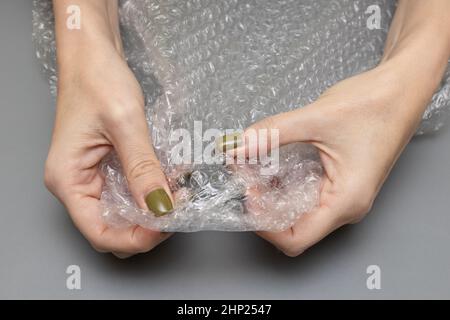 Frau platzt Blase wickeln in ihren Händen auf einem grauen Hintergrund. Hochwertige Fotos Stockfoto