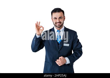 Schöner Mann in Uniform mit Abzeichen zeigt Schild ok auf weißem Hintergrund Stockfoto