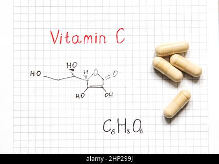 Chemische Formel von Vitamin C und einige Pillen auf dem weißen Papier Hintergrund. Nahaufnahme. Vitamine für die Gesundheit. Stockfoto