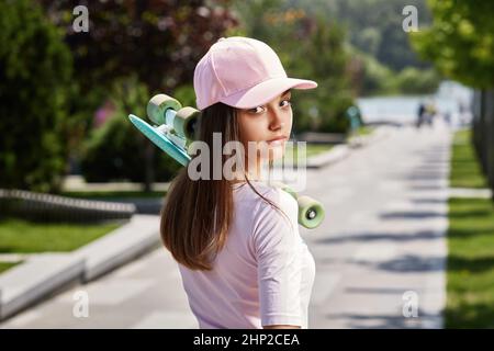 Junge schöne Brünette Skateboarderin Mädchen in Mütze mit Skateboard im Freien im Park stehen und mit Blick auf die Kamera Stockfoto