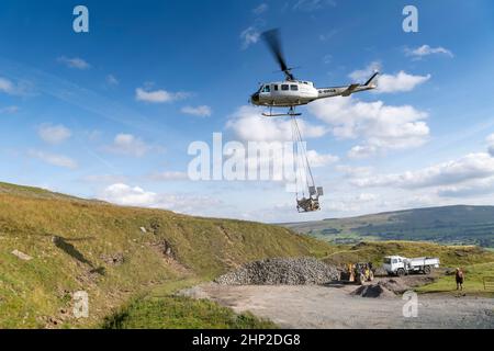 Hubschrauber, der eine Ladung Stein trägt, um auf das Moorland zu steigen, um bei der Wiederherstellung von Moor in den Yorkshire Dales, Großbritannien, zu helfen. Stockfoto