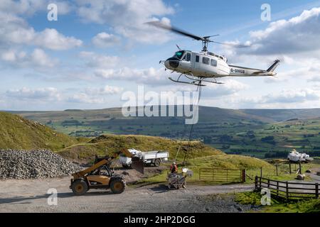 Hubschrauber, der eine Ladung Stein trägt, um auf das Moorland zu steigen, um bei der Wiederherstellung von Moor in den Yorkshire Dales, Großbritannien, zu helfen. Stockfoto