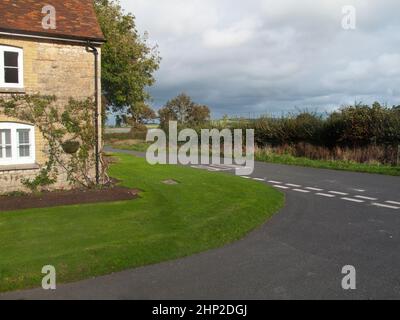 Ein Ferienhaus mit einem grünen Rasen an der Kreuzung einer Straße, umgeben von Büschen und Hecken Stockfoto