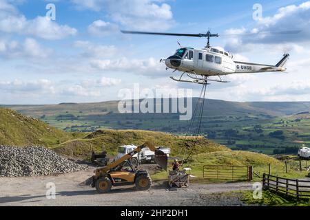 Hubschrauber, der eine Ladung Stein trägt, um auf das Moorland zu steigen, um bei der Wiederherstellung von Moor in den Yorkshire Dales, Großbritannien, zu helfen. Stockfoto