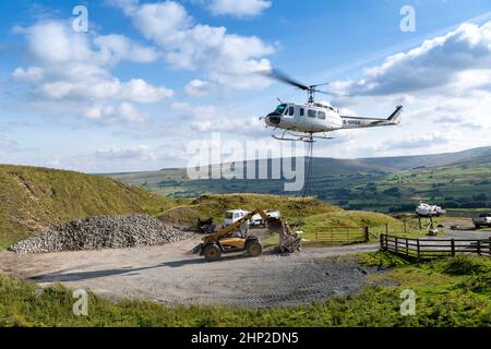 Hubschrauber, der eine Ladung Stein trägt, um auf das Moorland zu steigen, um bei der Wiederherstellung von Moor in den Yorkshire Dales, Großbritannien, zu helfen. Stockfoto