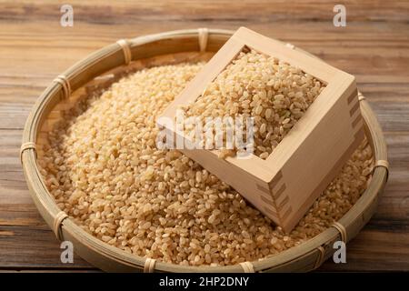 Brauner Reis in einer Holzkiste und Bambuskolander auf einem Holzhintergrund. Stockfoto