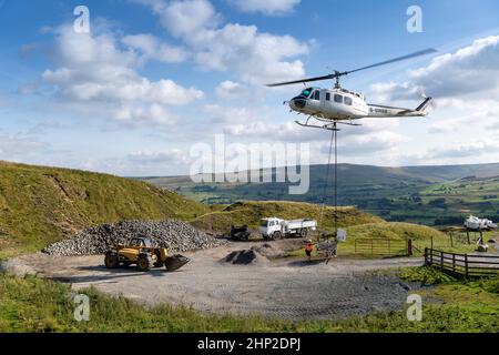 Hubschrauber, der eine Ladung Stein trägt, um auf das Moorland zu steigen, um bei der Wiederherstellung von Moor in den Yorkshire Dales, Großbritannien, zu helfen. Stockfoto