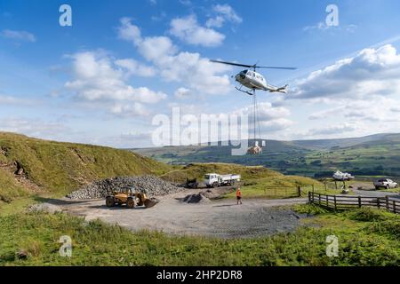 Hubschrauber, der eine Ladung Stein trägt, um auf das Moorland zu steigen, um bei der Wiederherstellung von Moor in den Yorkshire Dales, Großbritannien, zu helfen. Stockfoto