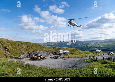 Hubschrauber, der eine Ladung Stein trägt, um auf das Moorland zu steigen, um bei der Wiederherstellung von Moor in den Yorkshire Dales, Großbritannien, zu helfen. Stockfoto