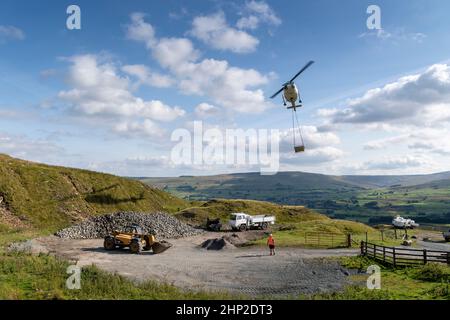 Hubschrauber, der eine Ladung Stein trägt, um auf das Moorland zu steigen, um bei der Wiederherstellung von Moor in den Yorkshire Dales, Großbritannien, zu helfen. Stockfoto