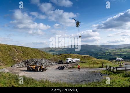 Hubschrauber, der eine Ladung Stein trägt, um auf das Moorland zu steigen, um bei der Wiederherstellung von Moor in den Yorkshire Dales, Großbritannien, zu helfen. Stockfoto